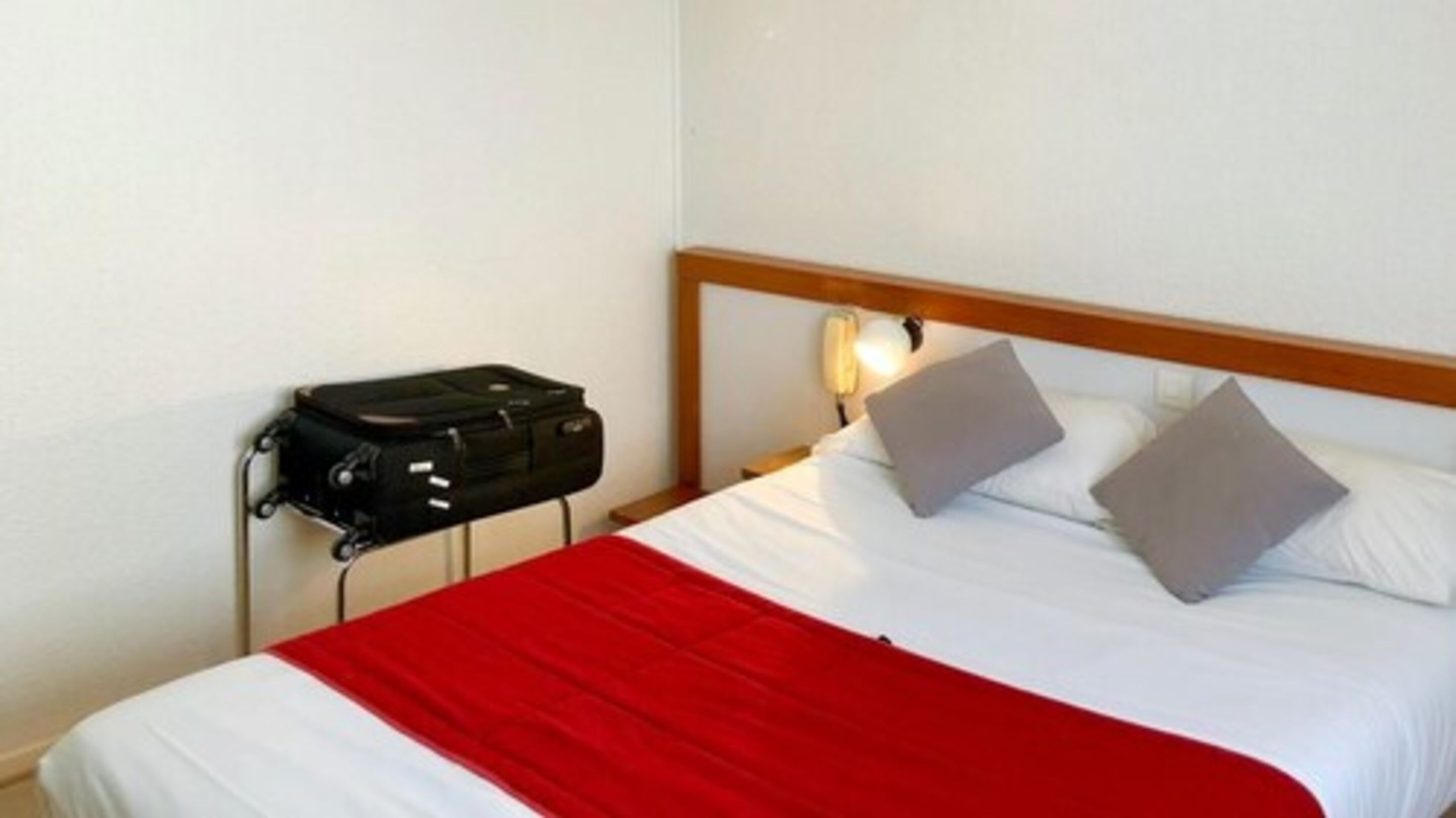 Une chambre d’hôtel avec un lit, une table de chevet, une lampe et une valise.