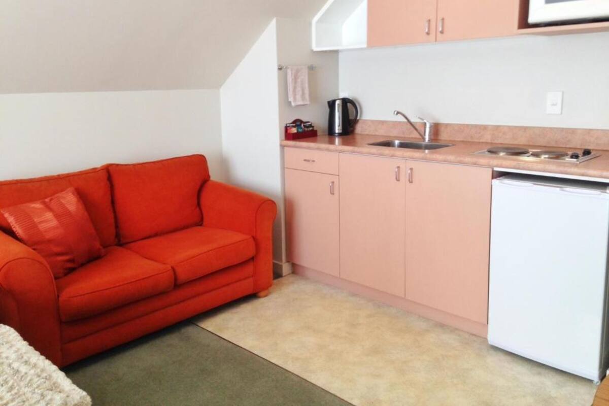 A compact kitchen with a red sofa, a microwave, a sink, and a small refrigerator.