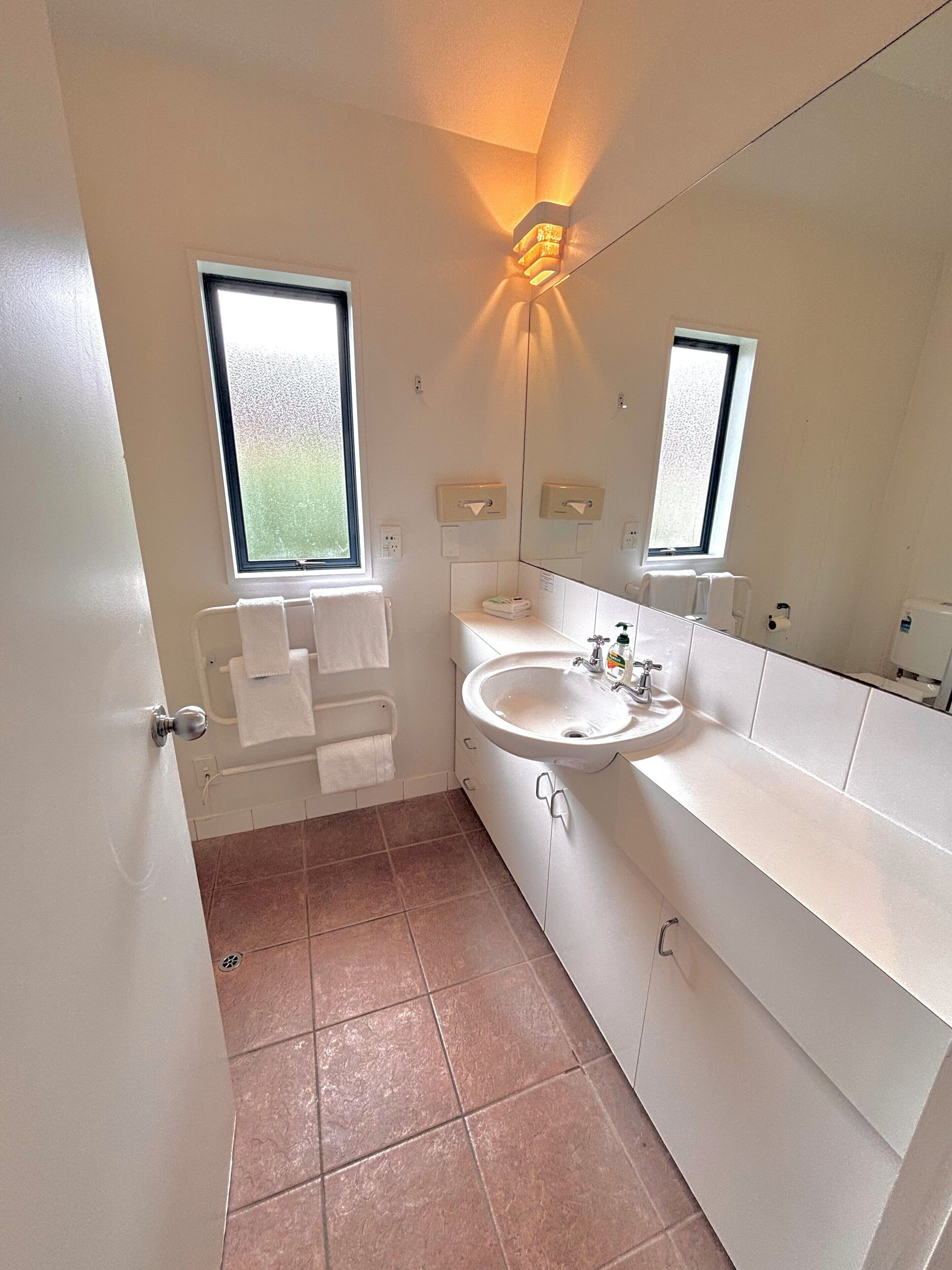 Une salle de bain moderne avec une grande fenêtre, un lavabo, un miroir et un porte-serviettes.