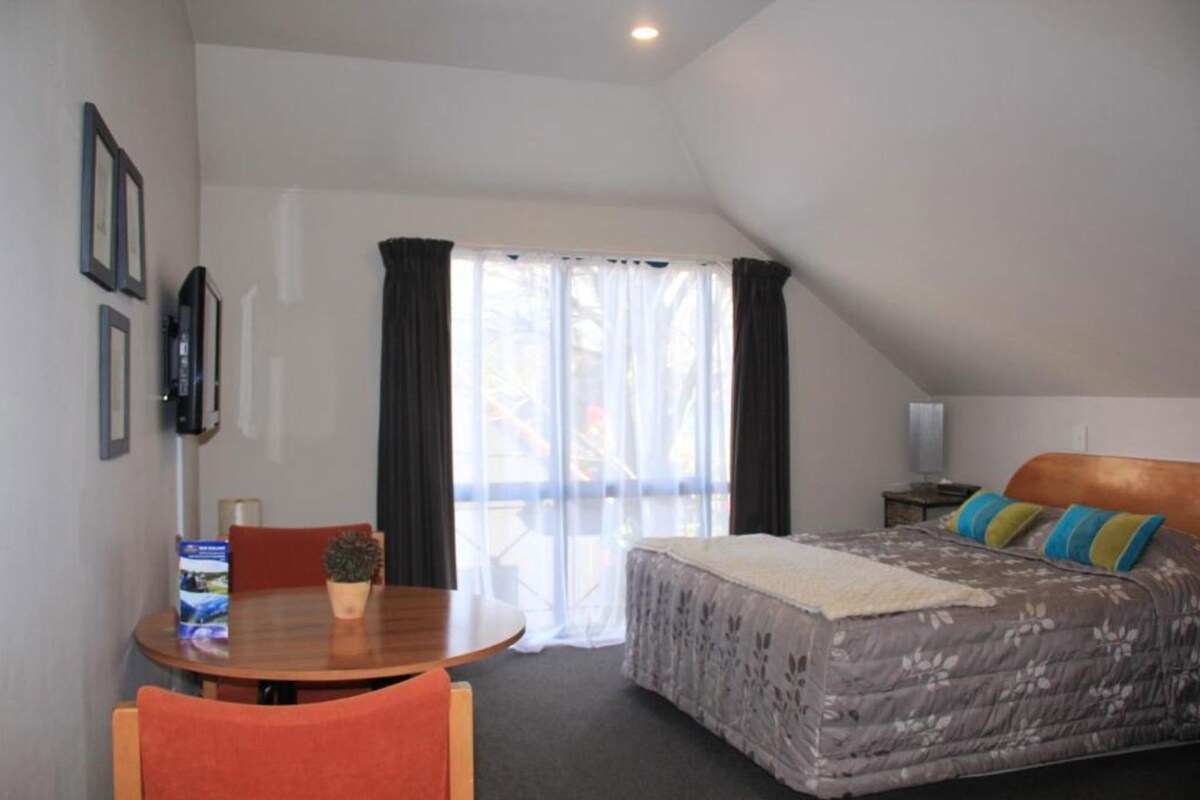 A bedroom with a bed, a desk, and a chair. There is a window with curtains.