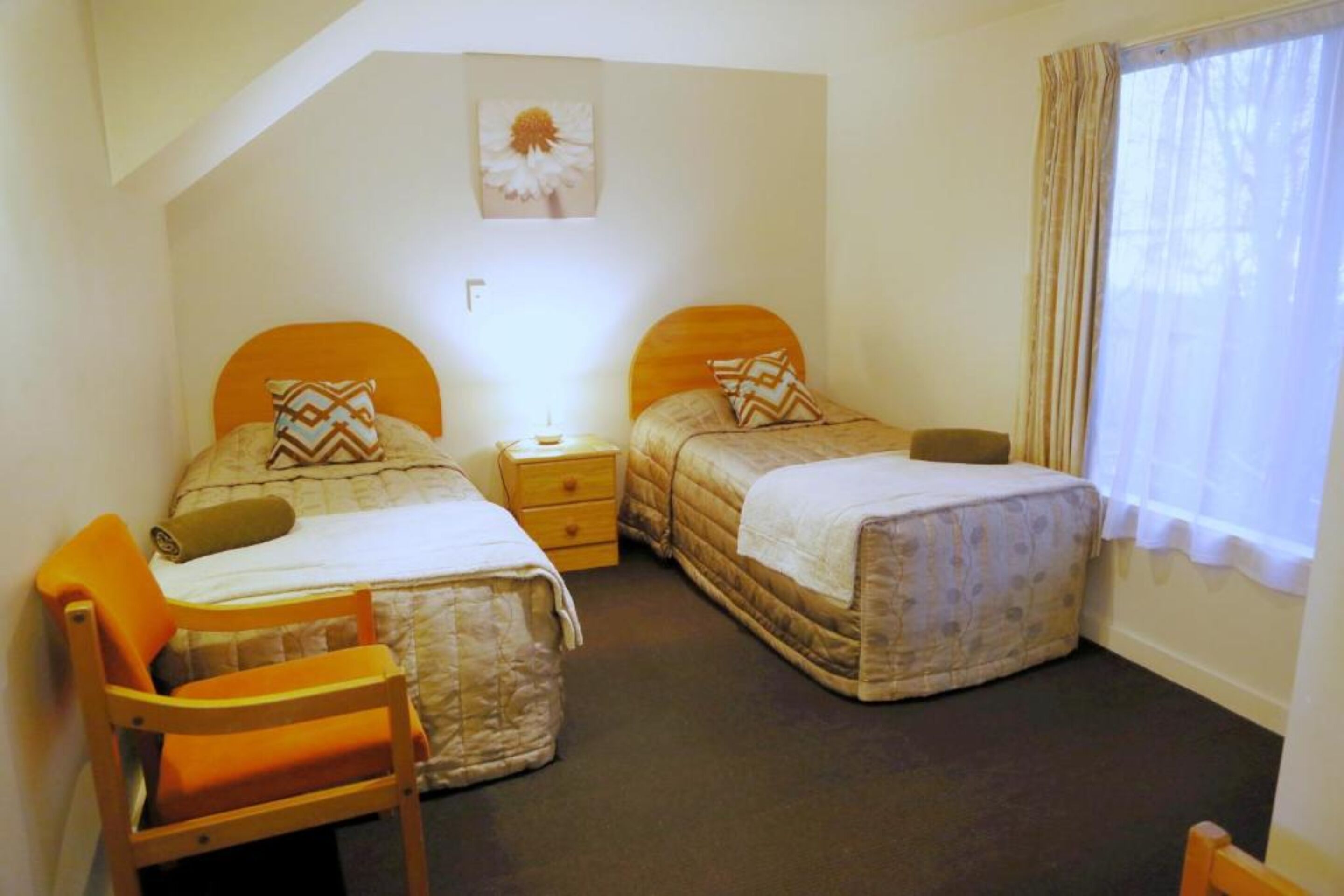 Une chambre avec deux lits, une chaise, une table de chevet et une fenêtre avec des rideaux.