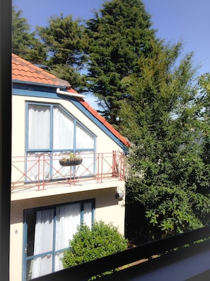 Ein zweistöckiges Gebäude mit rotem Ziegeldach, einem Balkon mit Geländer und einem Fenster mit weißen Vorhängen.