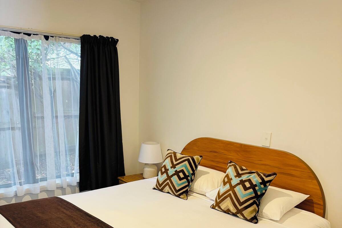 A neatly made bed with a brown throw blanket, two patterned pillows, and a wooden headboard.