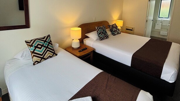 A hotel room with two single beds, each with a pillow, a bedside lamp, and a remote control on a wooden nightstand.