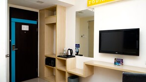 A hotel room with a black door, a wooden shelf unit, a black LG TV, and a small trash bin. - Zodiak Paskal by KAGUM Hotels (Bandung)