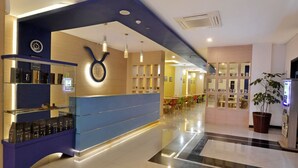 A modern hotel lobby with a reception desk, a large potted plant, and a seating area with tables and chairs. - Zodiak Paskal by KAGUM Hotels (Bandung)