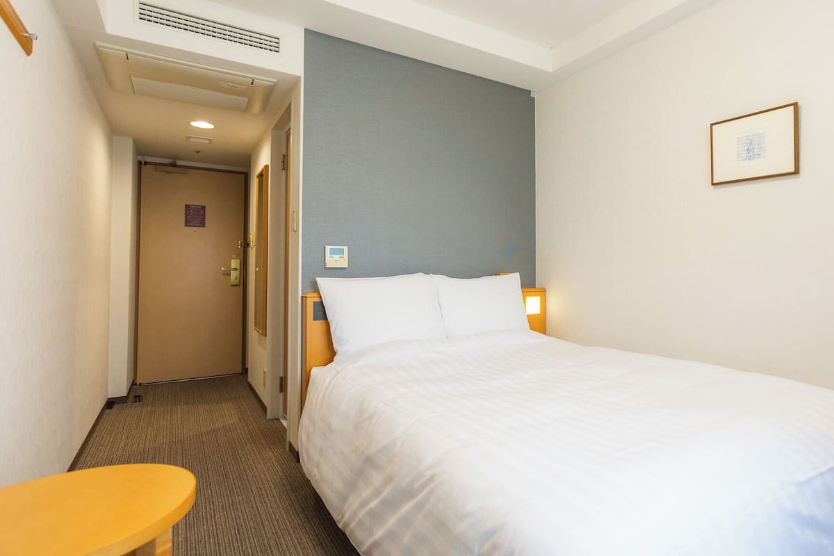 A hotel room with a bed, bedside table, and a door leading to another room.