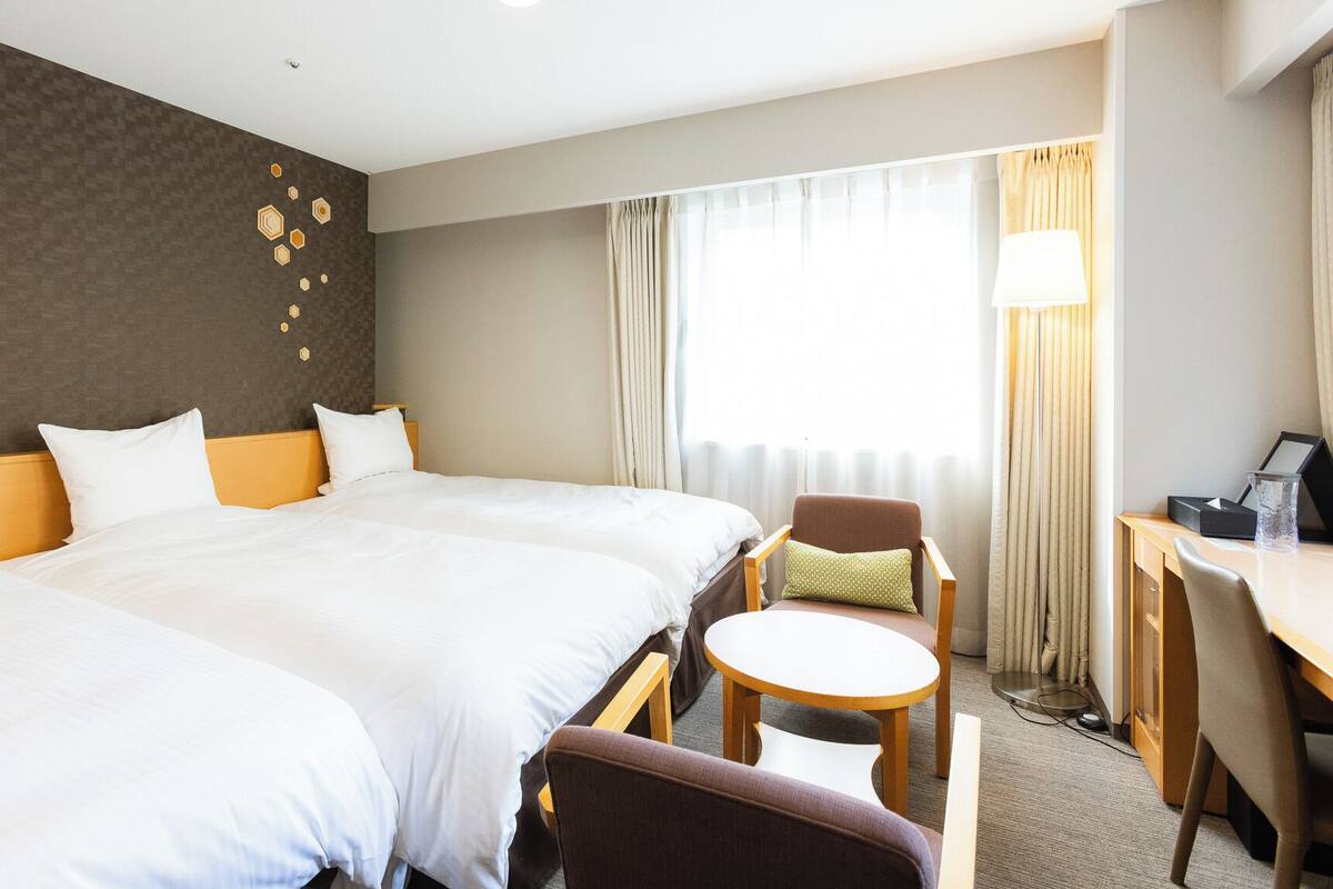 A hotel room with a large bed, a desk, a chair, and a small table.