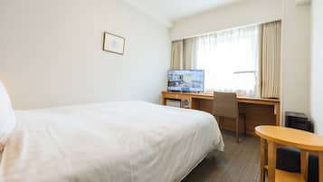Een hotelkamer met een bed, bureau, stoel, computer en raam met gordijnen.