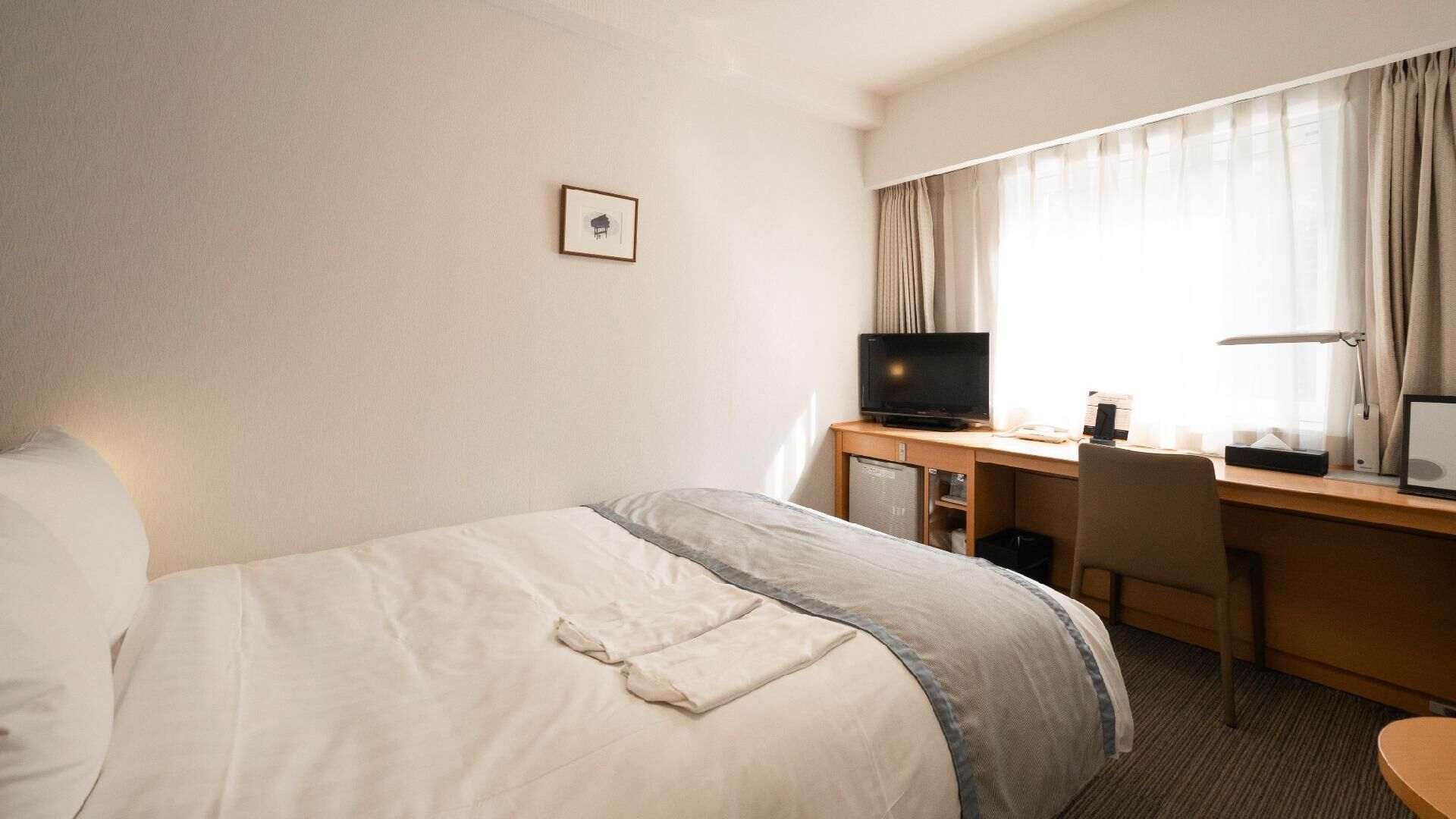 A hotel room with a bed, desk, television, and a picture on the wall.