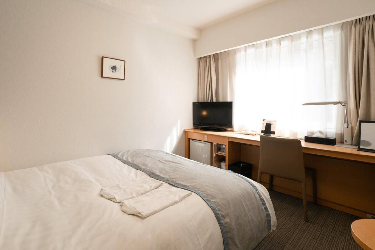 A hotel room with a bed, desk, television, and a picture on the wall.