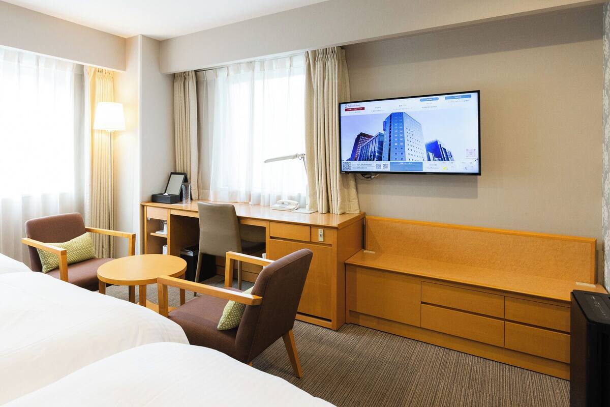 A hotel room with two beds, a desk, a chair, a TV, and a window with curtains.