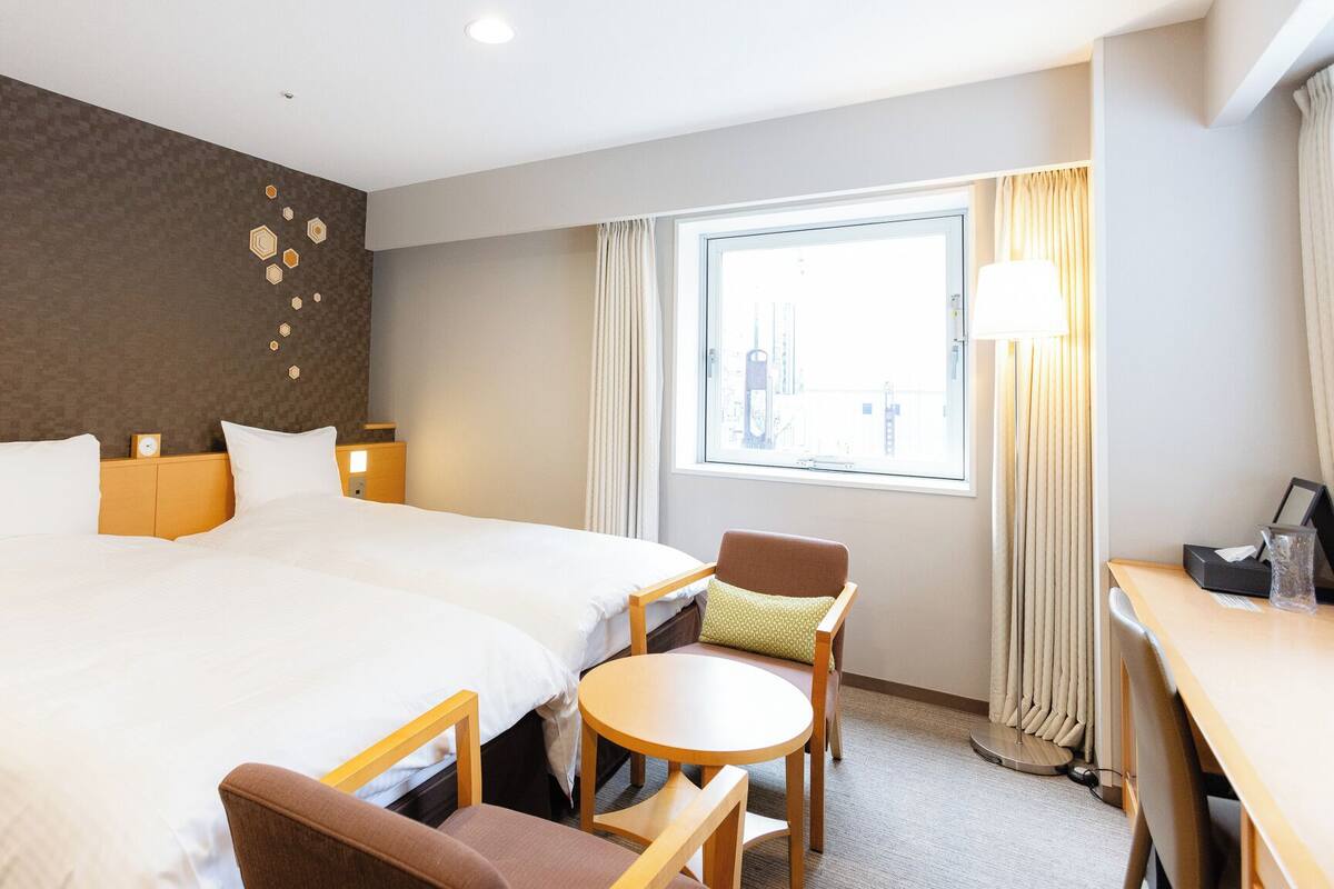 A hotel room with a large bed, a desk, a chair, and a window with curtains.