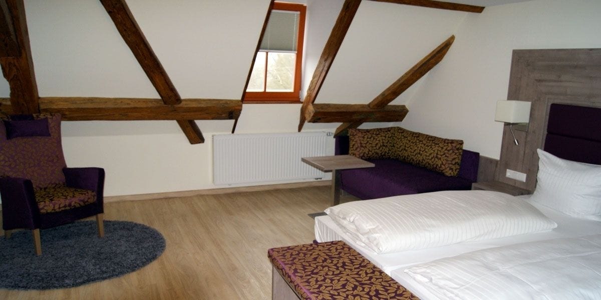 Un dormitorio con techo inclinado, una cama, una silla, una mesita y un radiador.