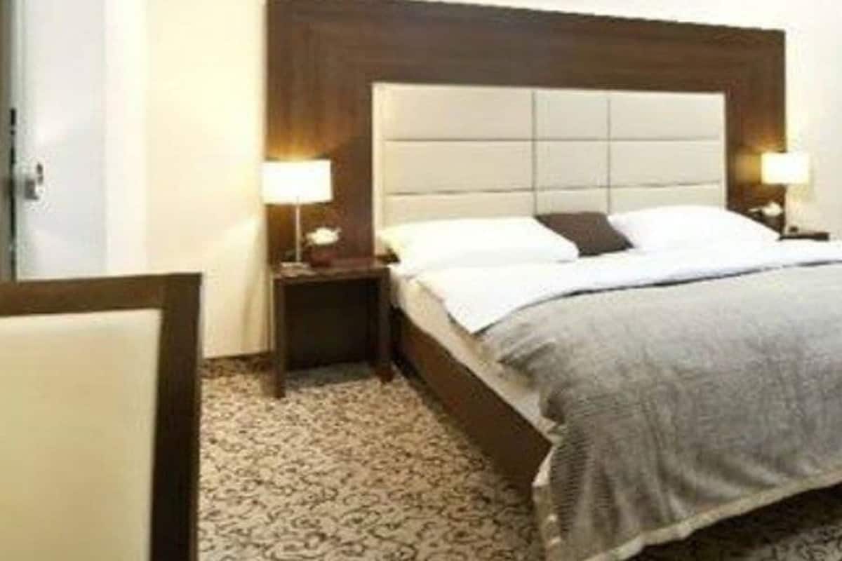 Ein Hotelzimmer mit einem Bett, zwei Nachttischen mit Lampen, einem Kopfteil und einem gemusterten Teppich.