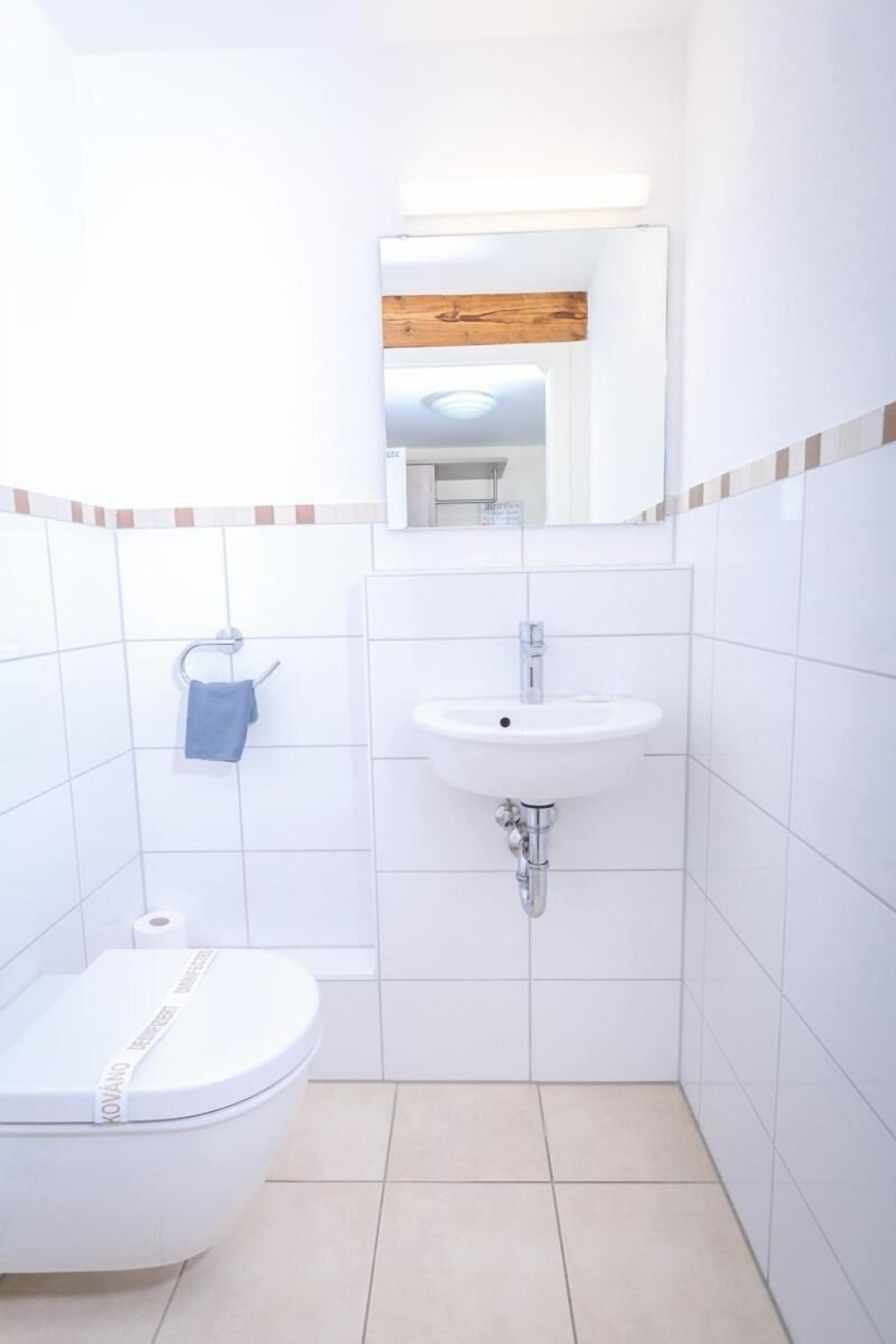 A small, white bathroom with a toilet, sink, and mirror.