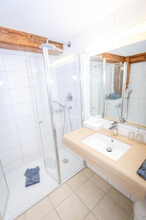 A modern bathroom with a glass shower enclosure, a wooden ceiling, a large mirror, and a beige tiled floor. - Sternen Hotel & Restaurant (Uhldingen-Muehlhofen)