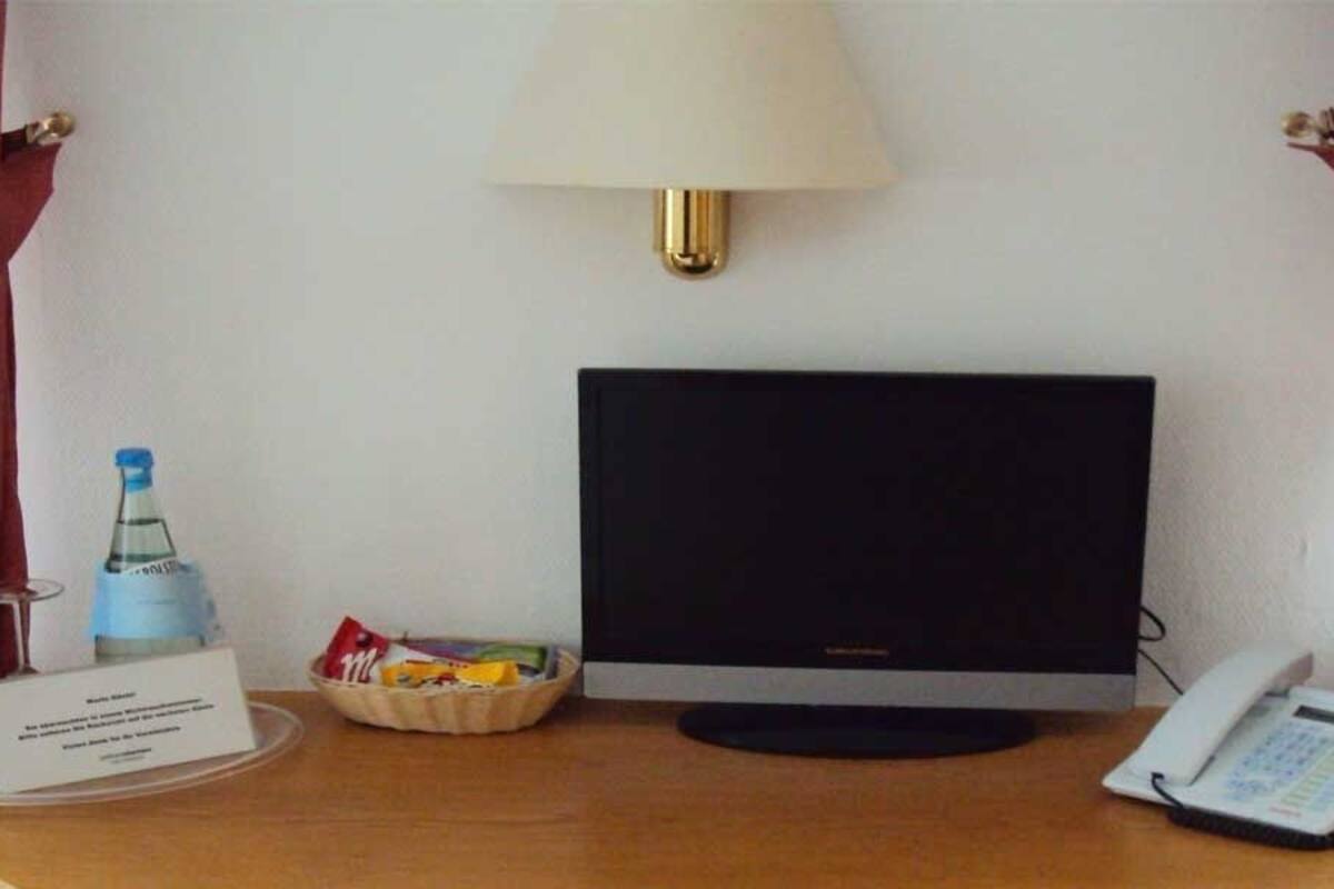 Ein Hotelzimmer mit Schreibtisch, Flachbildfernseher, Telefon, Wasserflasche und einer kleinen Snackauswahl.