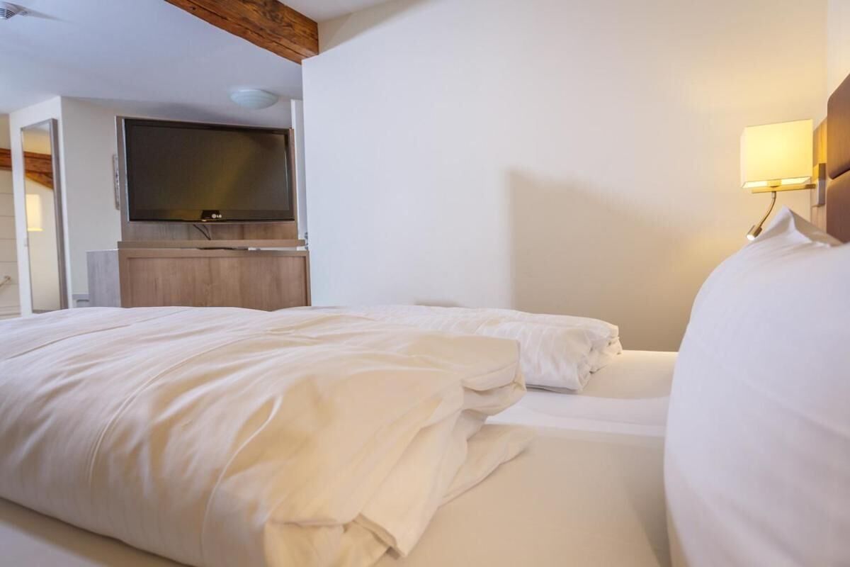 A hotel room with two beds, a TV, and a wall-mounted lamp.