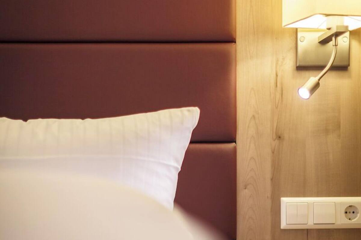 Ein Hotelzimmer mit einem großen Bett, einem Holzkopfstück, einem Nachttisch mit Lampe und einer Steckdose.