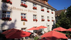 Un bâtiment portant l’enseigne « Gasthaus zum Sternen » et doté d’une terrasse avec des parasols rouges.