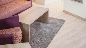 Une petite pièce accueillante, avec un canapé violet, une table basse en bois, une baignoire blanche et un miroir qui reflète un canapé à motifs.