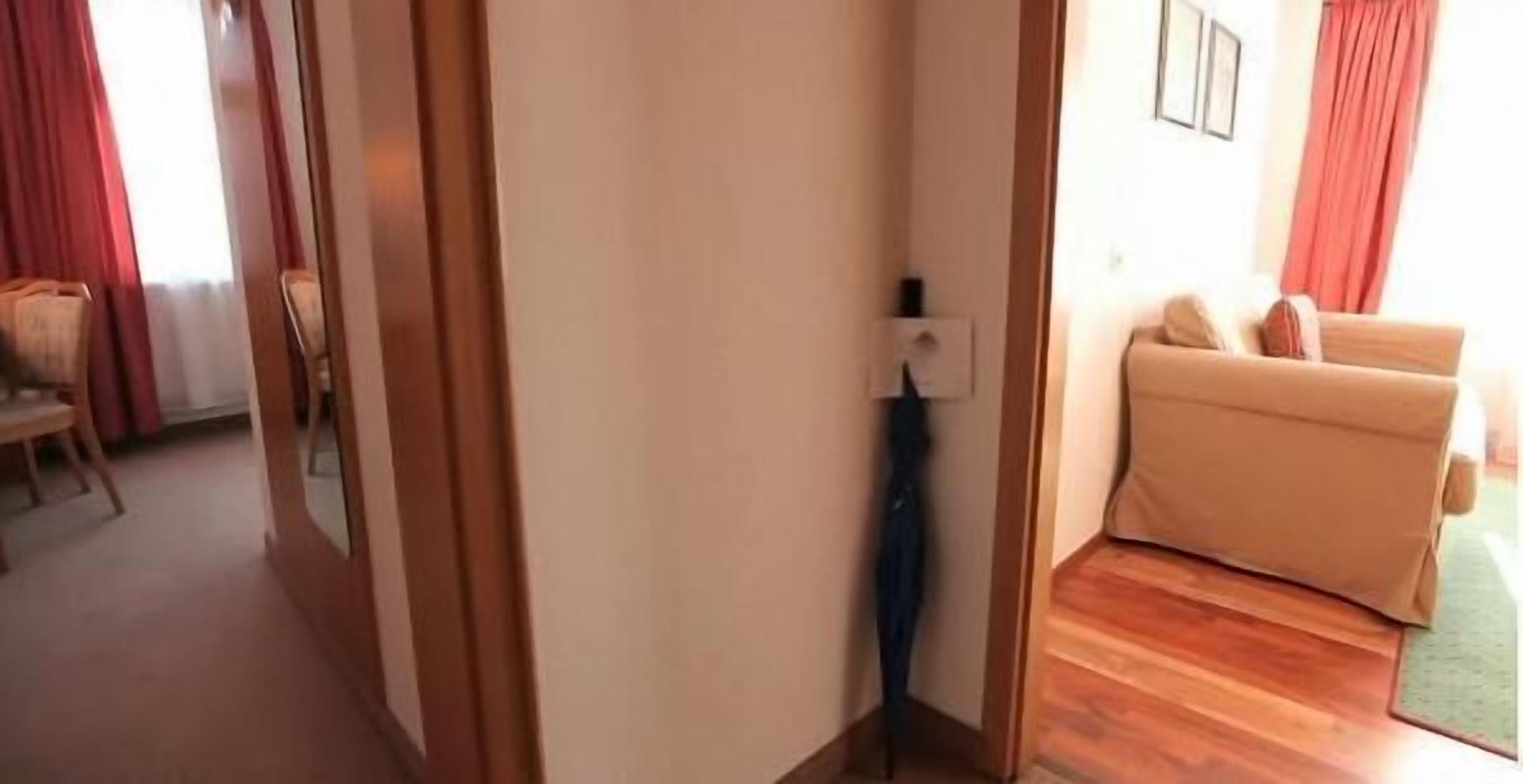 Una habitación con piso de madera, un sofá color crema y una silla. Hay una puerta que conduce a otra habitación.