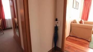 Una habitación con piso de madera, un sofá color crema y una silla. Hay una puerta que conduce a otra habitación.