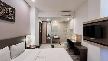 A modern hotel room with a large bed, a desk, a TV, and a bathroom visible through an open door.