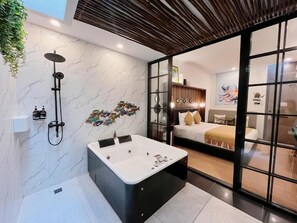 A modern bathroom with a large bathtub, a shower, and a glass door leading to a bedroom. - Oak Tree Urban Jakarta (Jakarta)