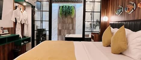 Habitación de hotel con cama, escritorio, silla, armario y baño visible a través de una puerta abierta.