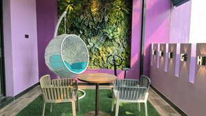 A modern lounge area with a hanging chair, two chairs, a round table, and a wall with vertical light fixtures. - Oak Tree Urban Jakarta (Jakarta)