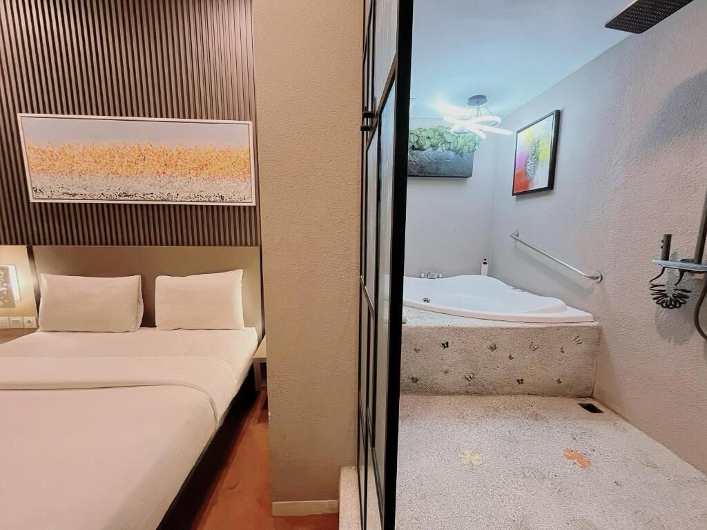A hotel room with a bed, a small bathroom with a bathtub, and a painting on the wall.
