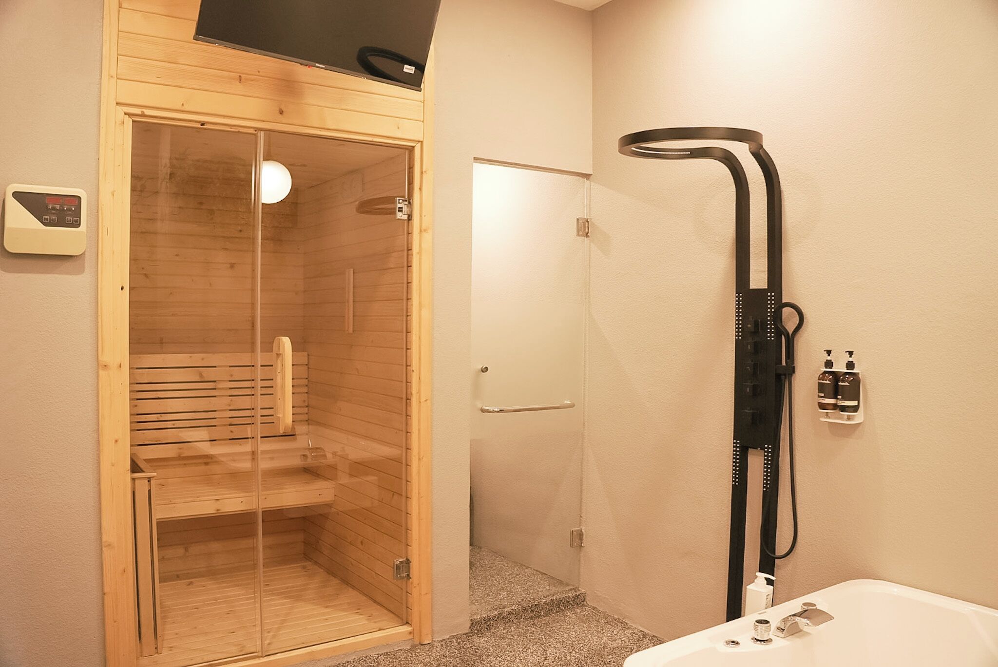 A modern bathroom with a glass-enclosed sauna, a black showerhead, and a control panel on the wall.