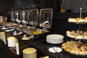 Enjoy a diverse selection of dishes at our buffet, featuring a variety of hot and cold options, accompanied by fresh baked goods and fine tableware.