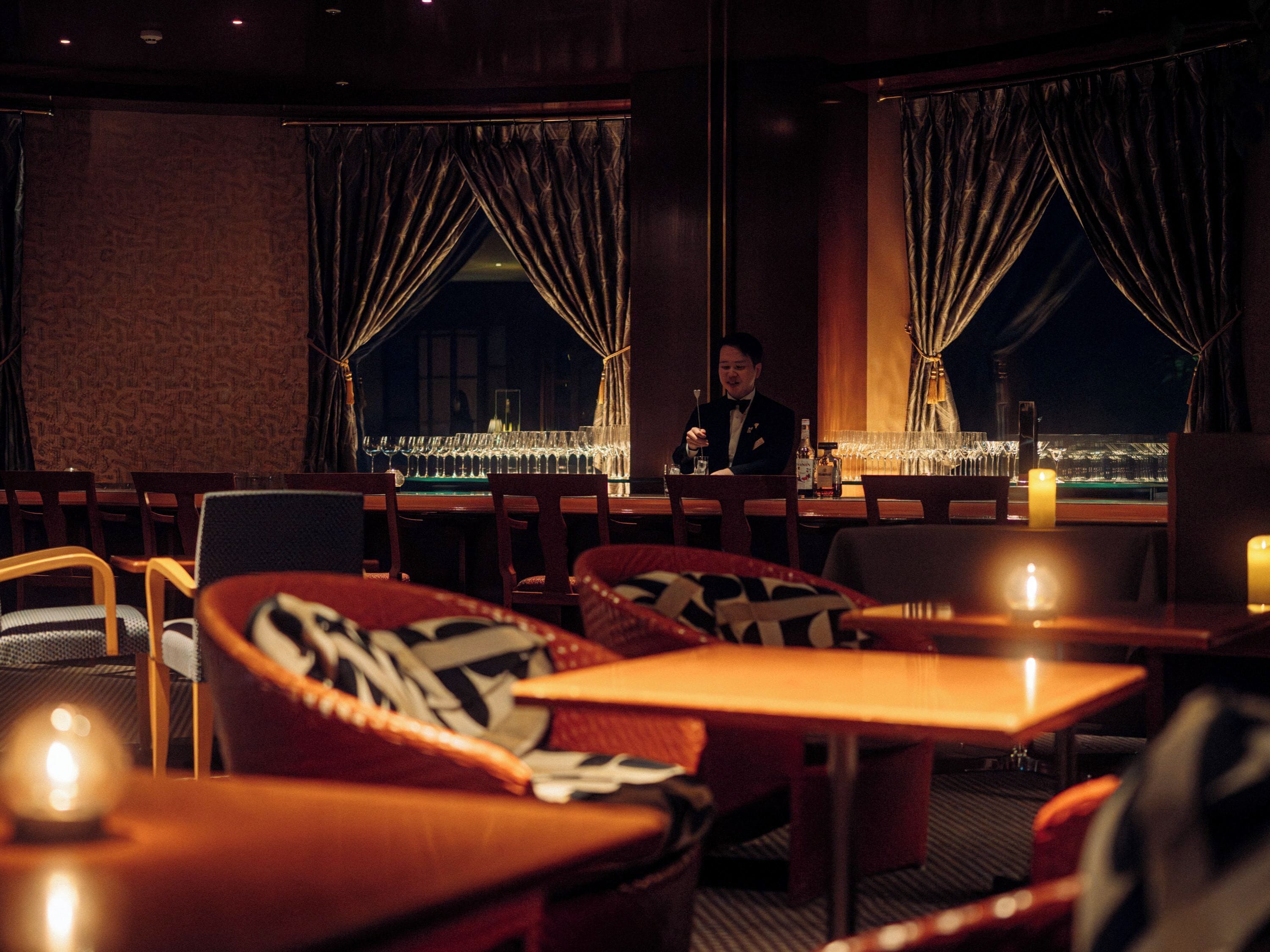 A dimly lit restaurant with a bar area, wooden chairs, and tables.