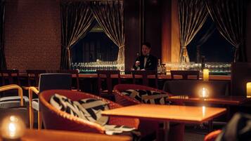 A dimly lit restaurant with a bar area, wooden chairs, and tables.