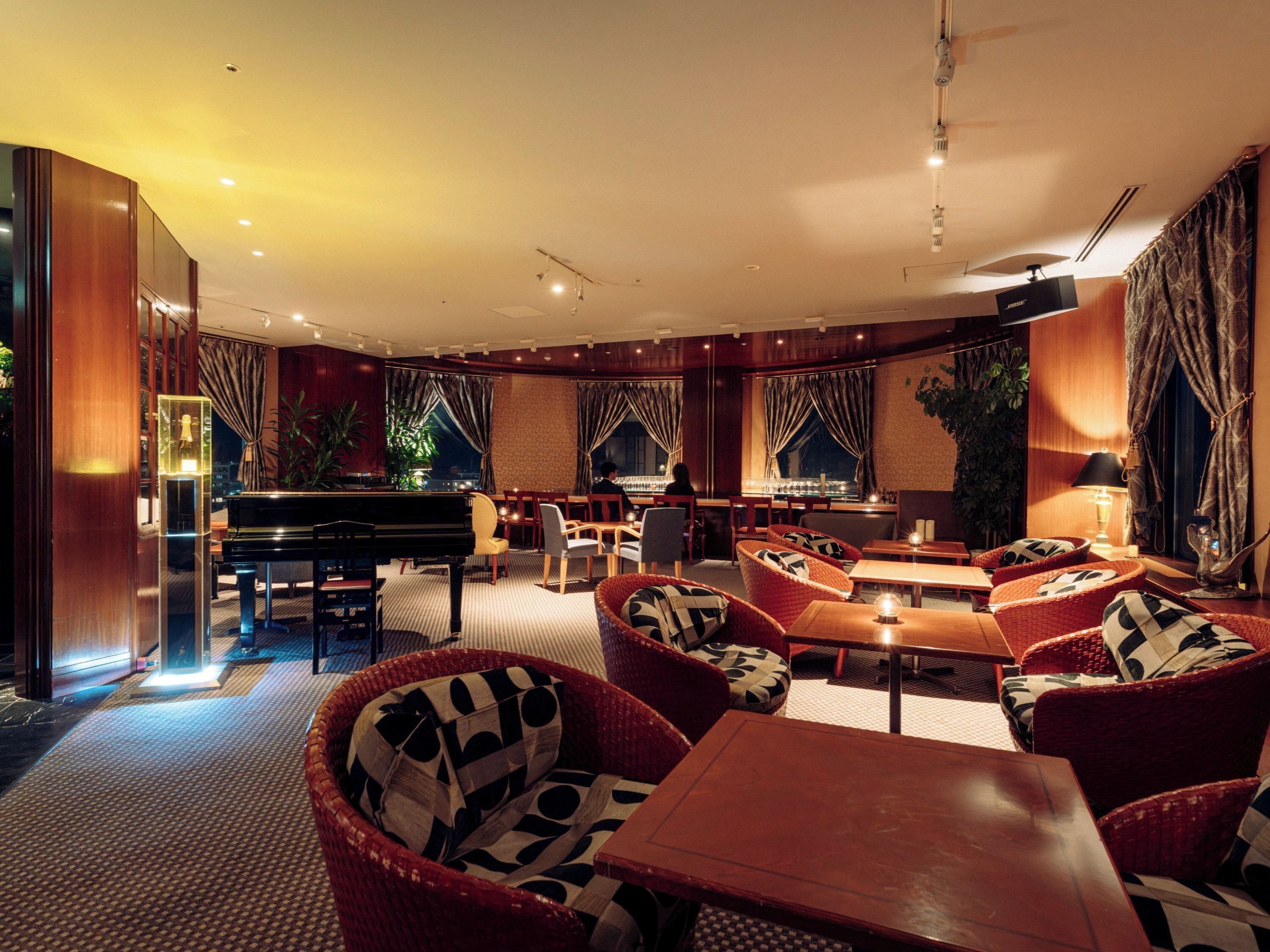 A hotel lobby with a grand piano, comfortable seating, a bar area, and large windows with curtains.