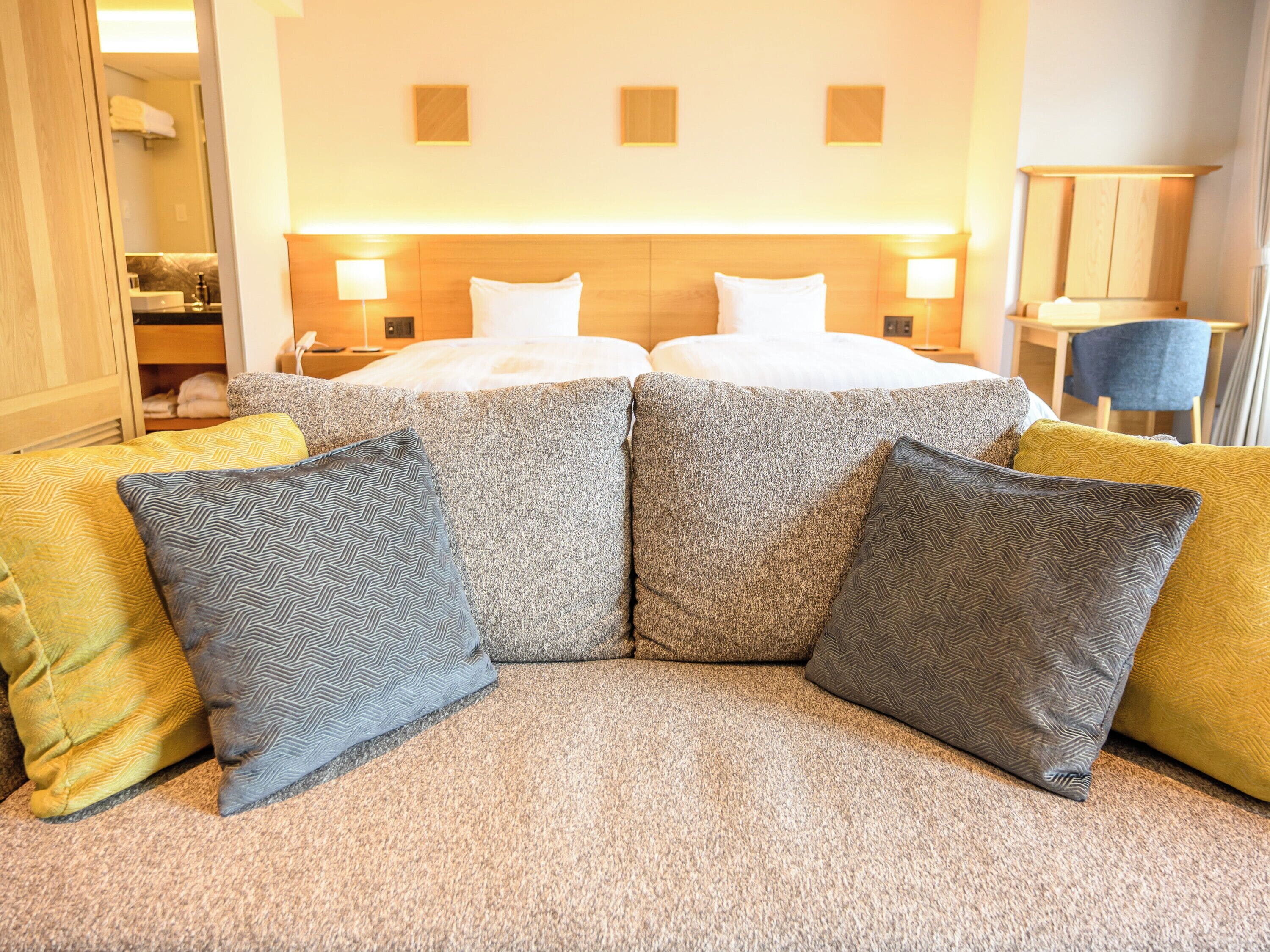 A hotel room with a large bed, two bedside tables with lamps, a sofa with patterned cushions, and a wooden headboard.