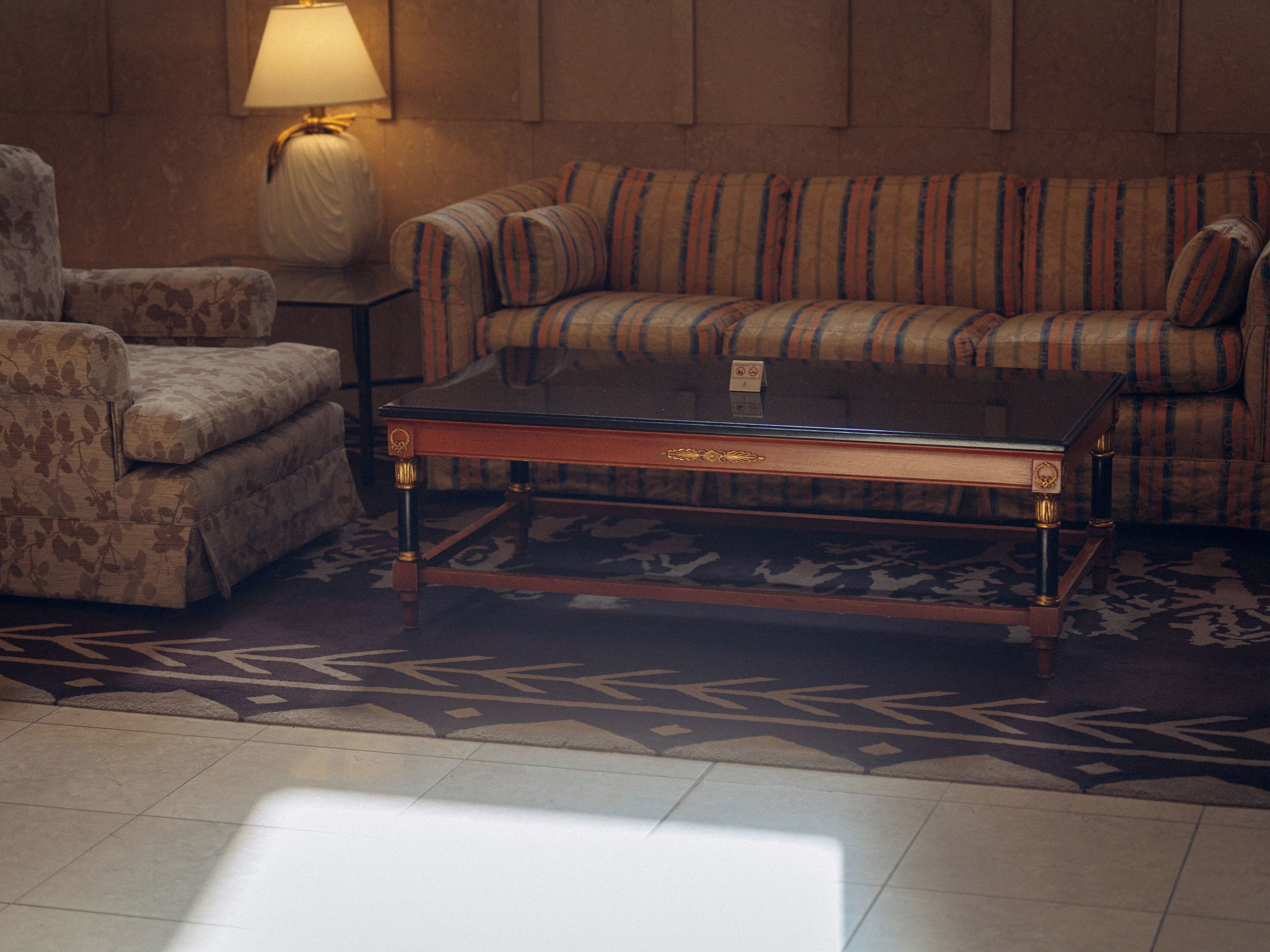 Una habitación con sofá a rayas, sillón floral, una mesa de centro de vidrio, una lámpara y alfombra estampada.