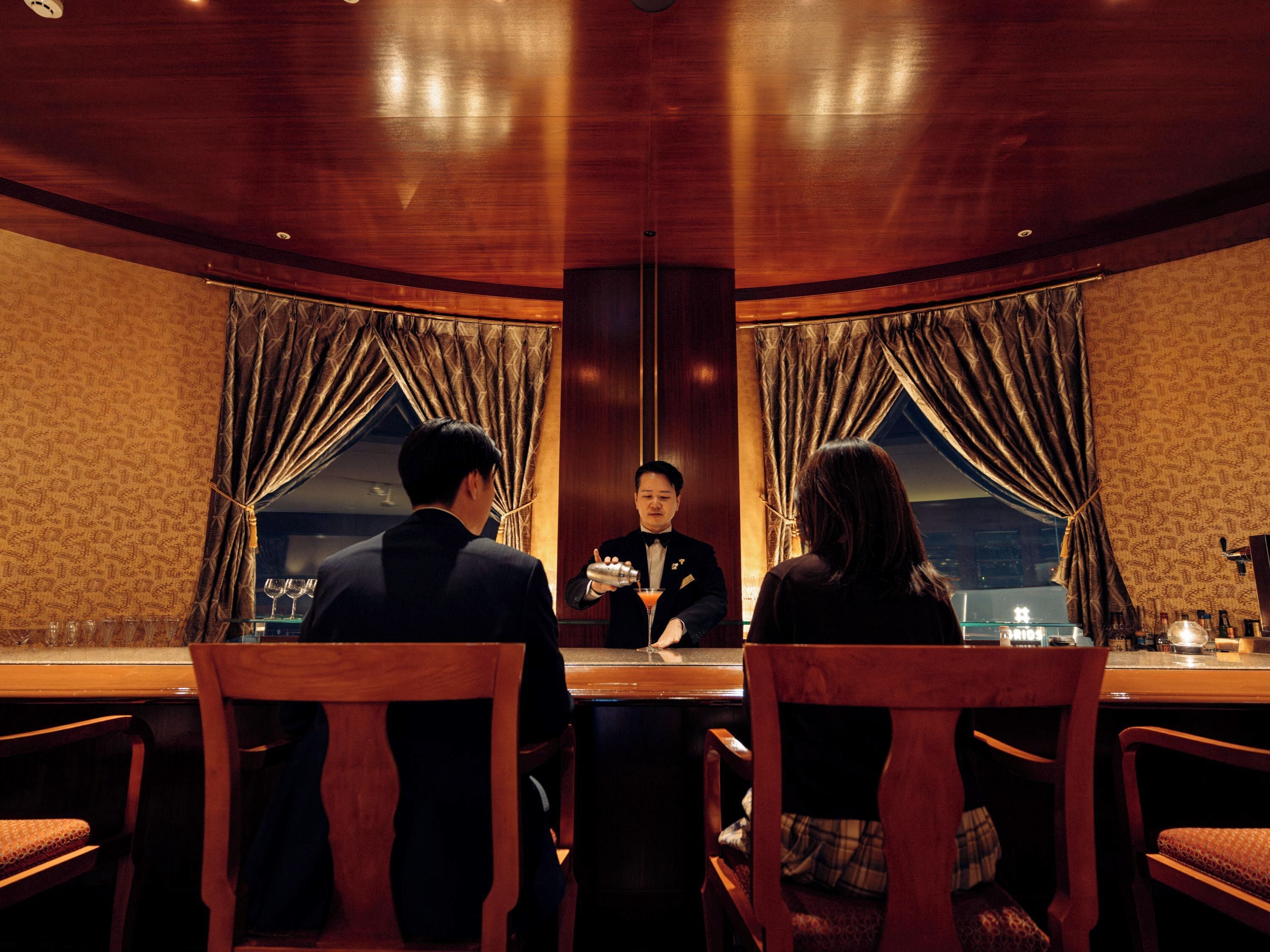A round table with four chairs, a waiter, and a view of the night sky through large windows.