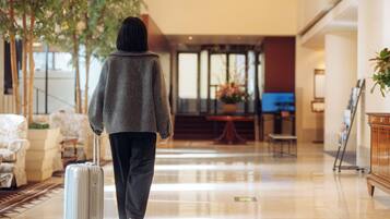 A person walking with a suitcase in a hotel lobby with a plant, a reception desk, and a seating area.