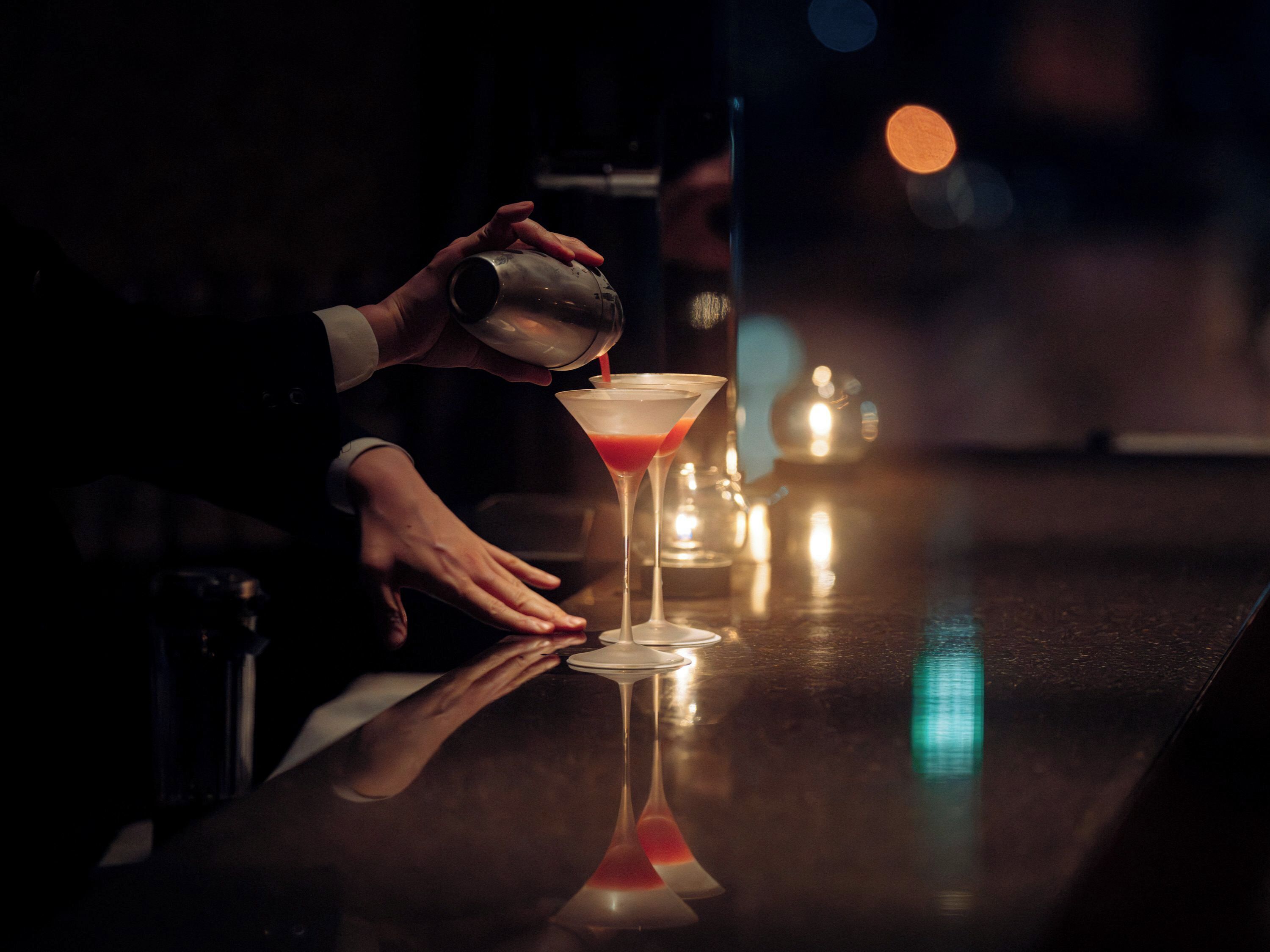Un bar con una persona sirviendo una bebida en una copa de martini.