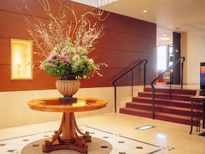 A lobby with a round wooden table, a potted plant, a staircase, and a wall-mounted light fixture.