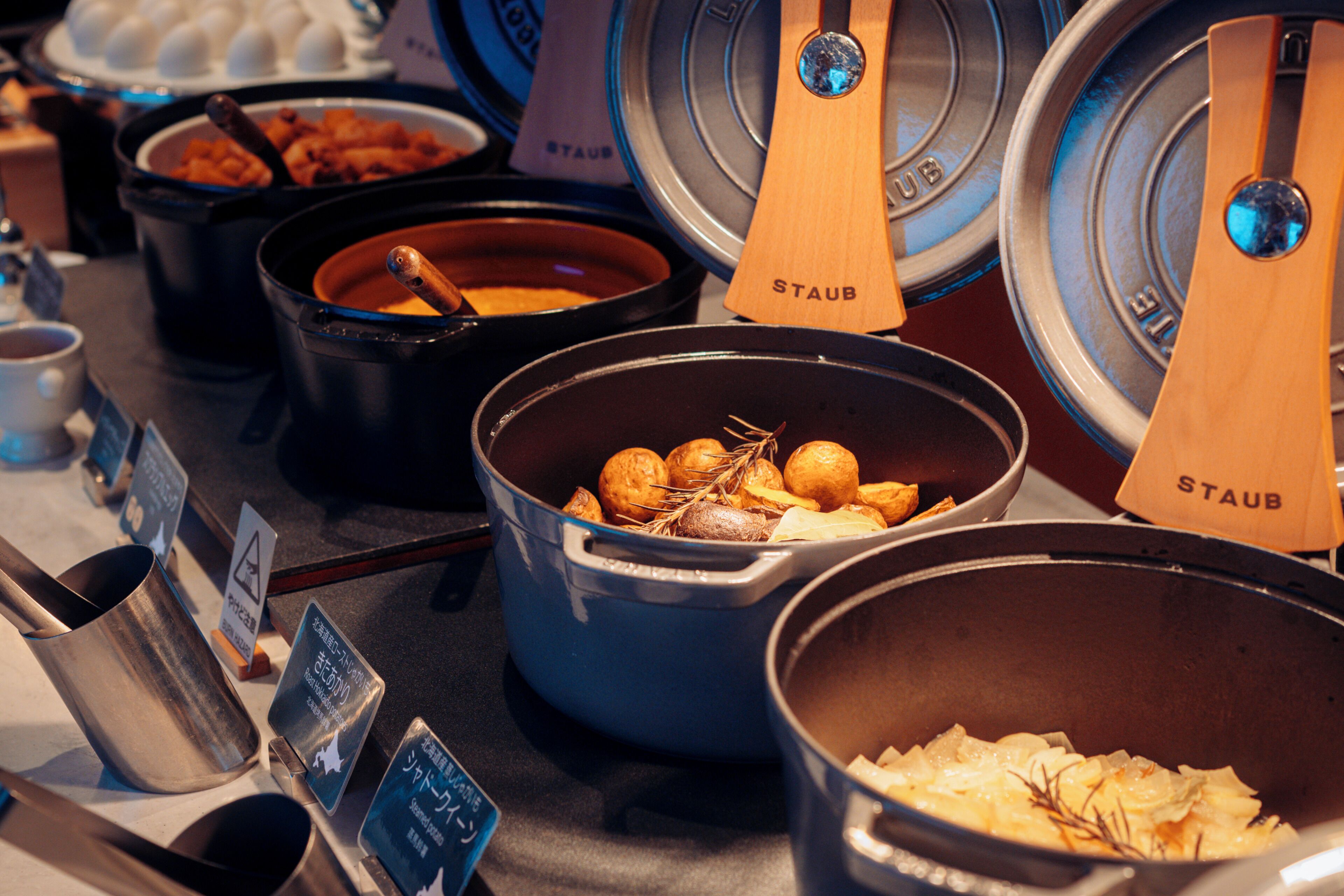 A buffet with various dishes in black and blue pots, some labeled 'STAUB'.