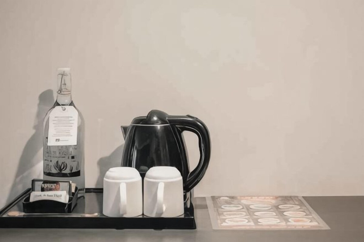 A coffee maker, two mugs, a bottle, and a tray on a table.