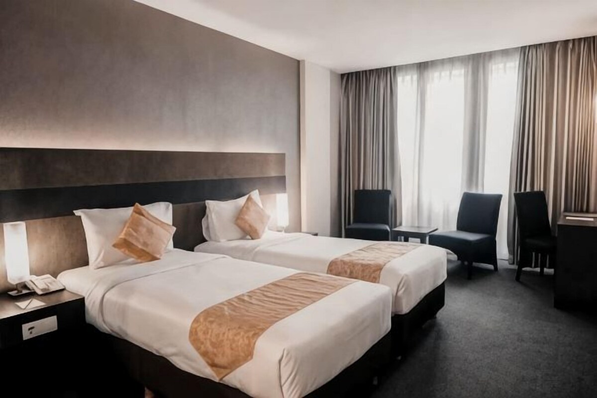 Une chambre d’hôtel avec deux lits, un bureau, une chaise et une grande fenêtre avec des rideaux.