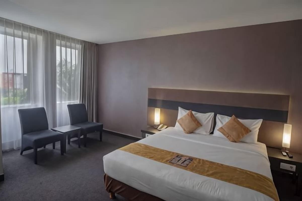 Ein Hotelzimmer mit einem großen Bett, Nachttischen, einem Schreibtisch und Stühlen.