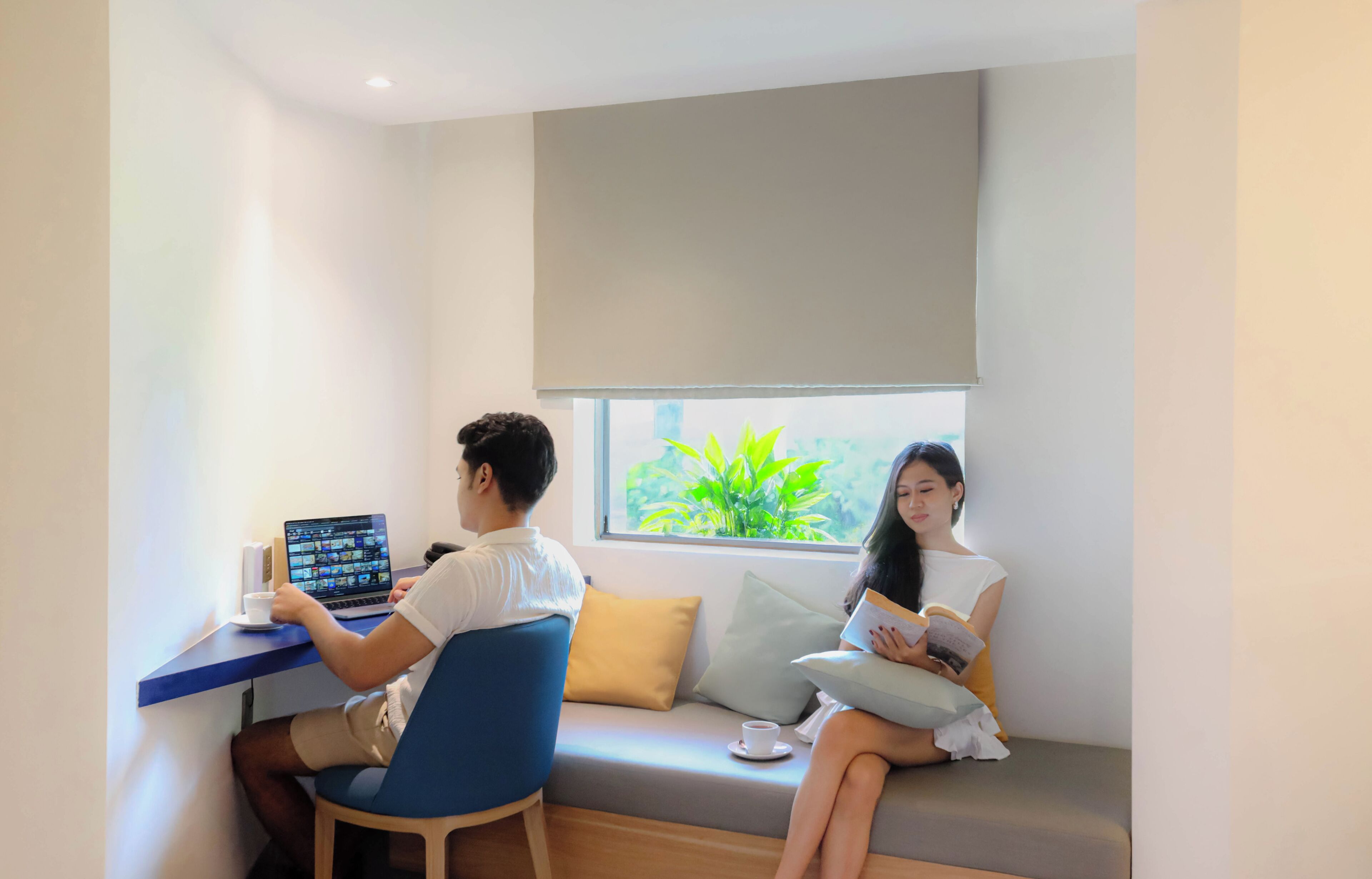 A room with a desk, a sofa, a window with a view of greenery, and a ceiling light.