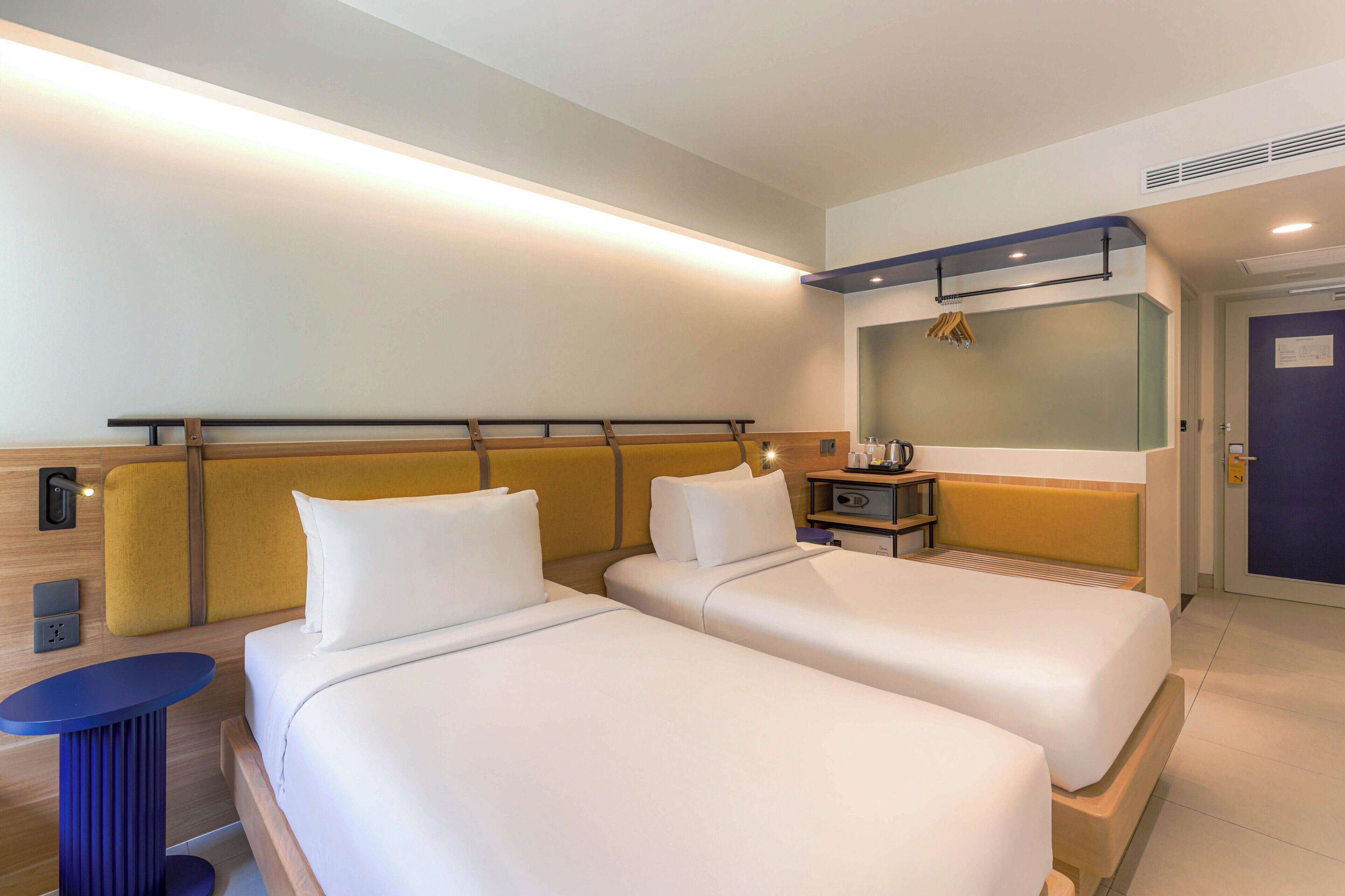 A hotel room with two beds, a small table, a mirror, and a door.